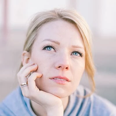 Blonde woman with blue eyes looking up, resting chin on hand