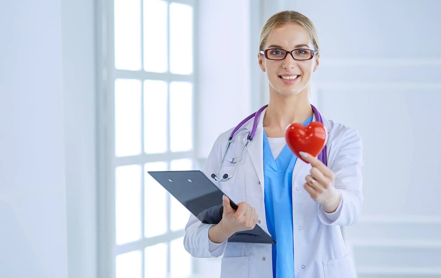 Smiling female doctor holding a red heart and a clipboard.